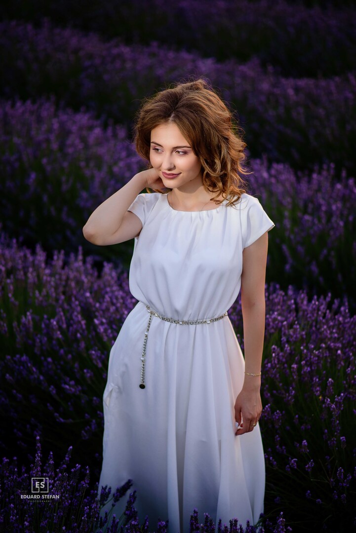 Portrait of a serene woman in a white dress standing amidst vibrant lavender fields, radiating elegance and natural beauty.