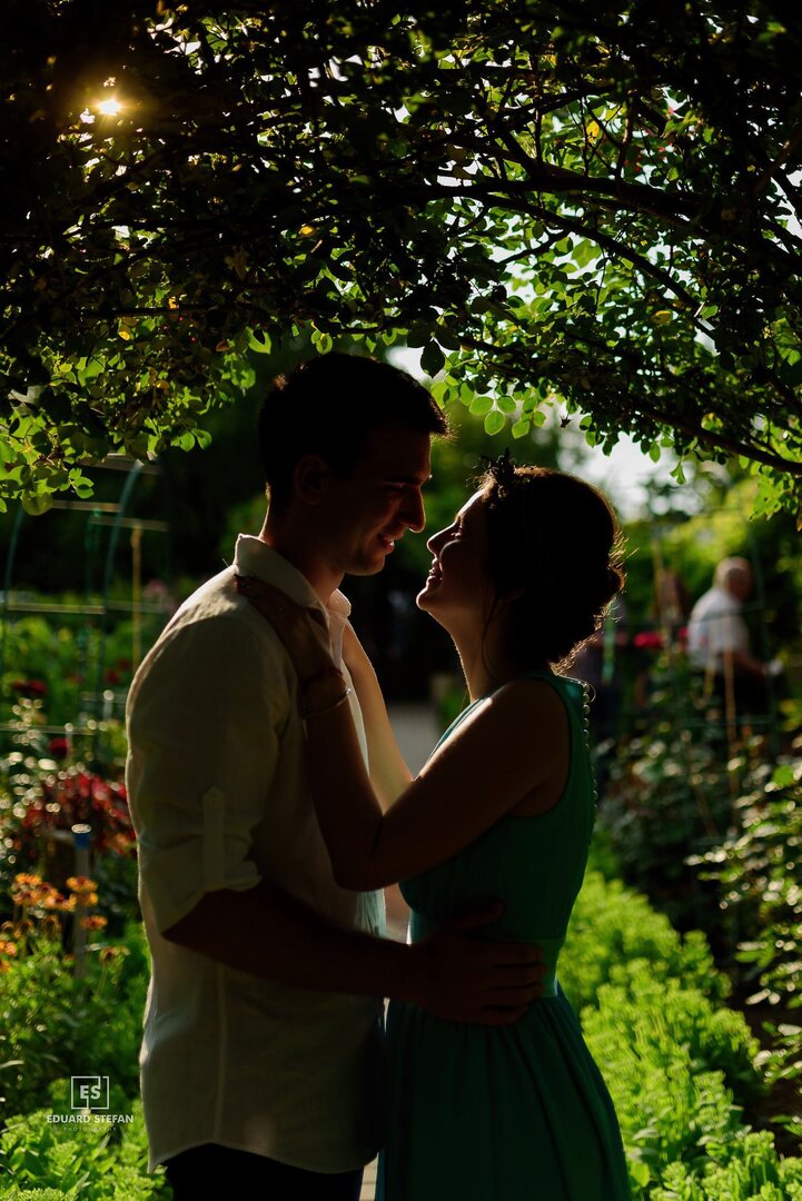 Couple sharing an intimate moment under a leafy archway in a sunlit garden.